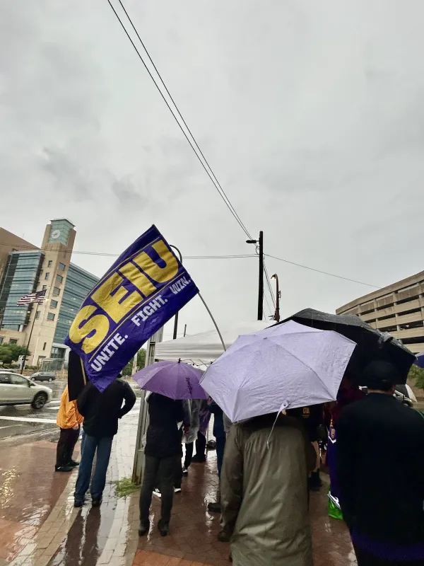 workers hold info picket rally in the pouring rain, morning of july 31, 2026 in downtown minneapolis - worker holds SEIU unite, fight, win flag as others rally while holding signs and umbrellas